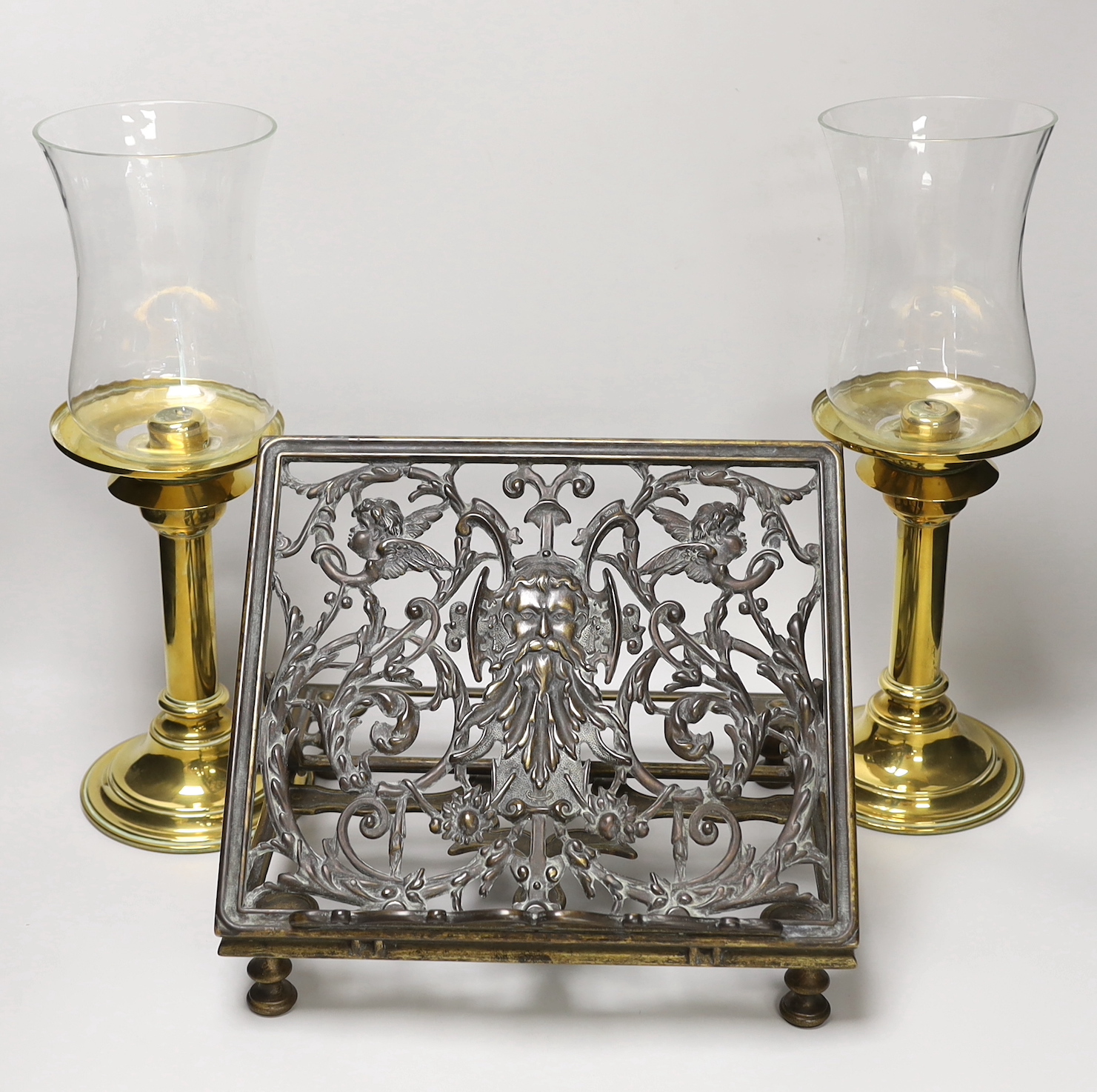 A pair of brass candlesticks with spring loading actions and storm shades and a Victorian cast brass adjustable reading stand with pierced and embossed decoration, the largest each 37cm high